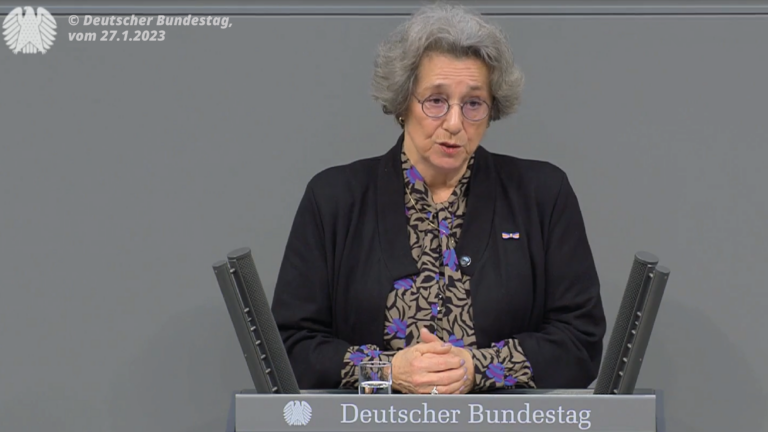 Gedenken an die Opfer des Nationalsozialismus: Eine Frau mit grauen Haaren und Brille steht vor einem Rednerpult. Sie hat ihre Hände vor sich auf dem Pult gefaltet.