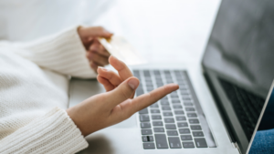 Eine Frau sitzt an einem Laptop. Es sind nur der Laptop und ihre Hände zu sehen. Ihre Handhaltung deutet an, dass sie am Laptop mit einer Person spricht.